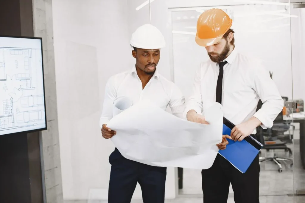 Two professionals in hard hats reviewing architectural blueprints